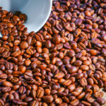 Šálka ​​čerstvo pripravenej kávy s kávovými zrnami v pozadí, zdôrazňujúca bohatú arómu.