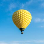 Žltý teplovzdušný balón stúpajúci do modrej oblohy – magický pohľad a jedinečný zážitok z letu balónom.