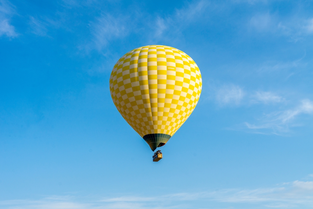Žltý teplovzdušný balón stúpajúci do modrej oblohy – magický pohľad a jedinečný zážitok z letu balónom.